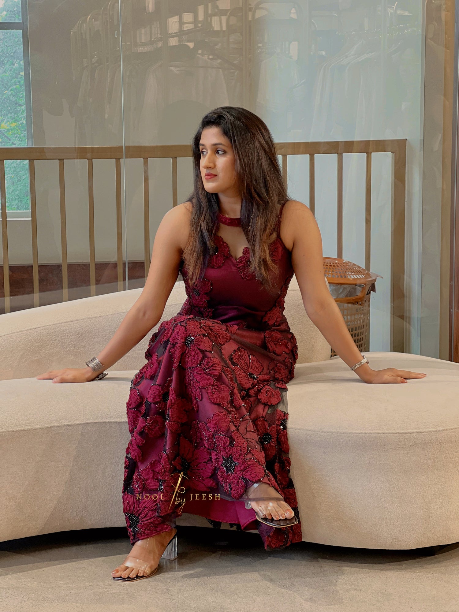 Woman in a red floral dress sitting on a beige sofa indoors.